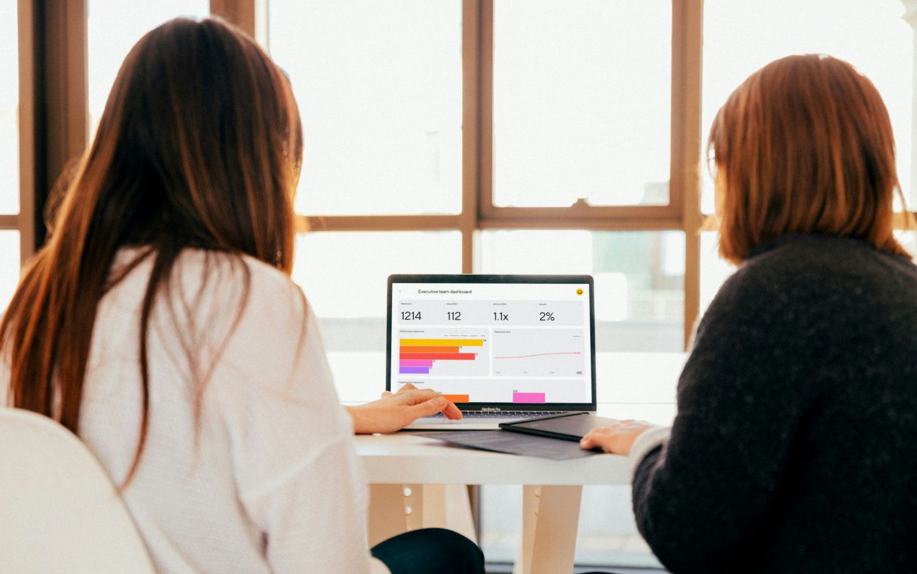 Over-the-shoulder shot of two people looking at a Dandi dashboard on a laptop.